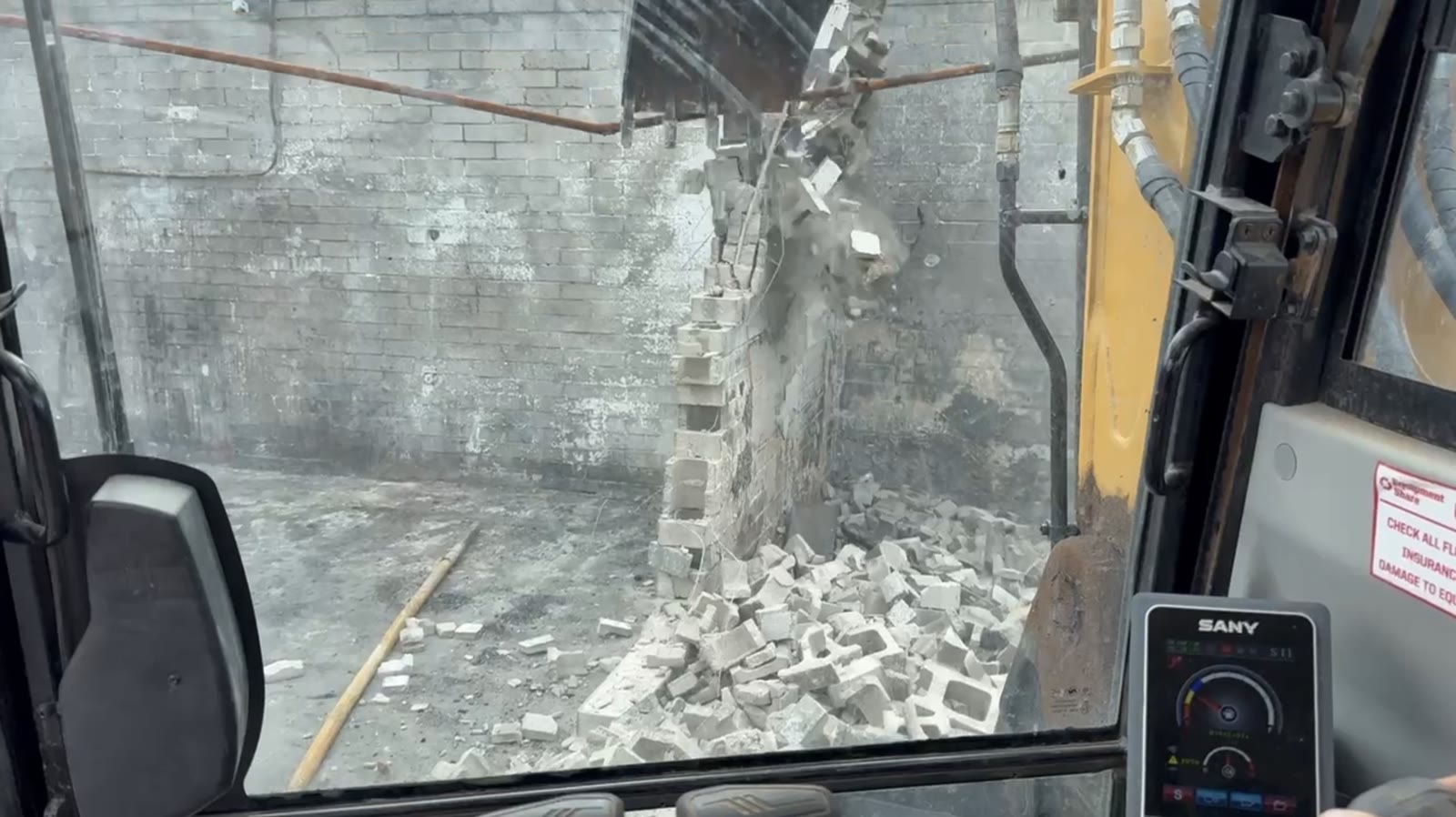 Excavator breaking down a concrete block wall