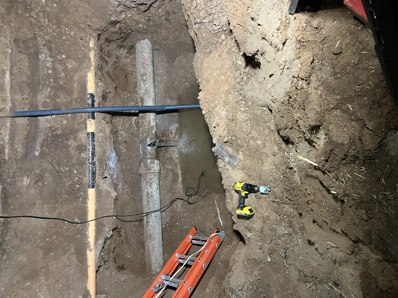 Open trench with concrete sewer pipe leak and utility line