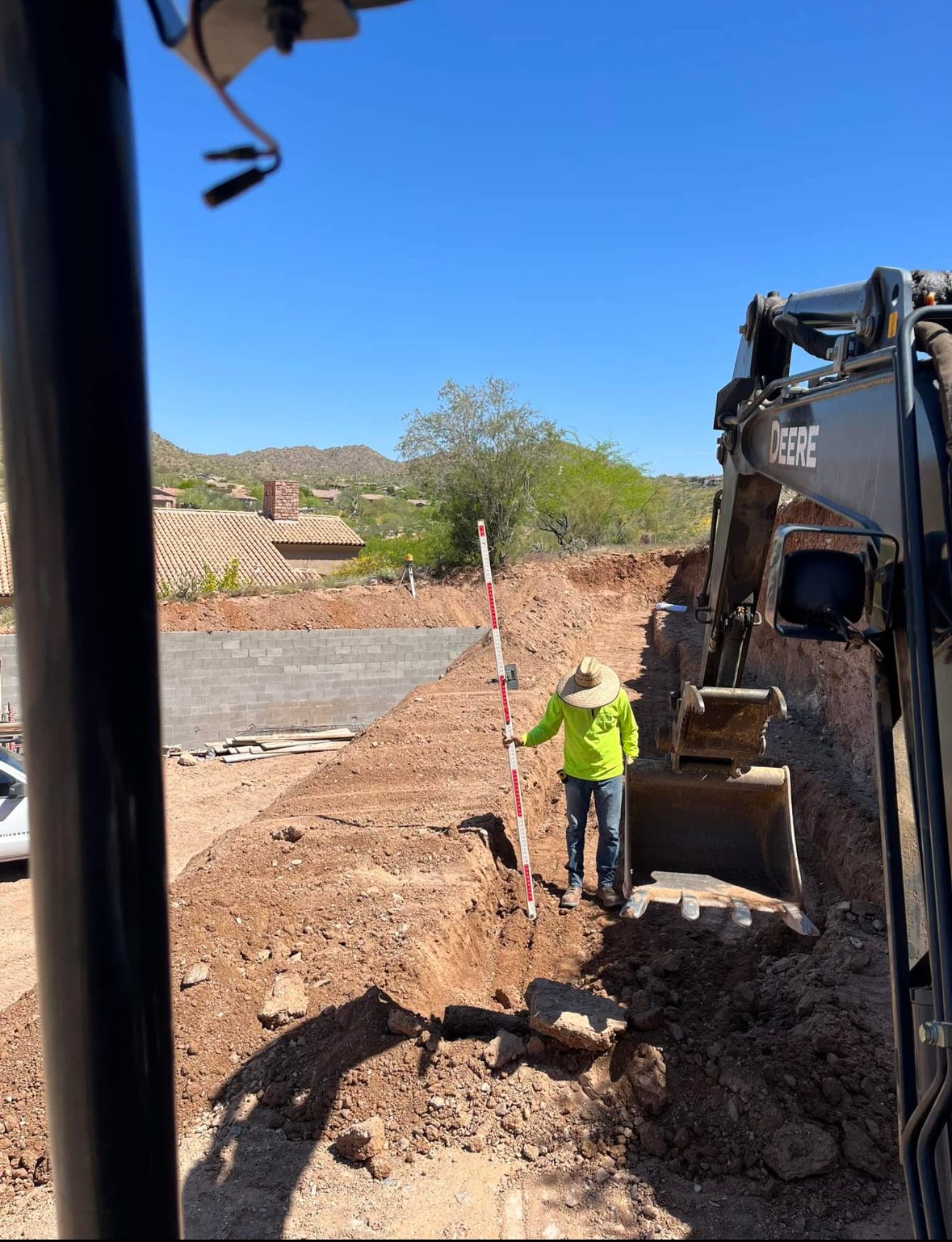 Worker checking grade with rod beside excavator