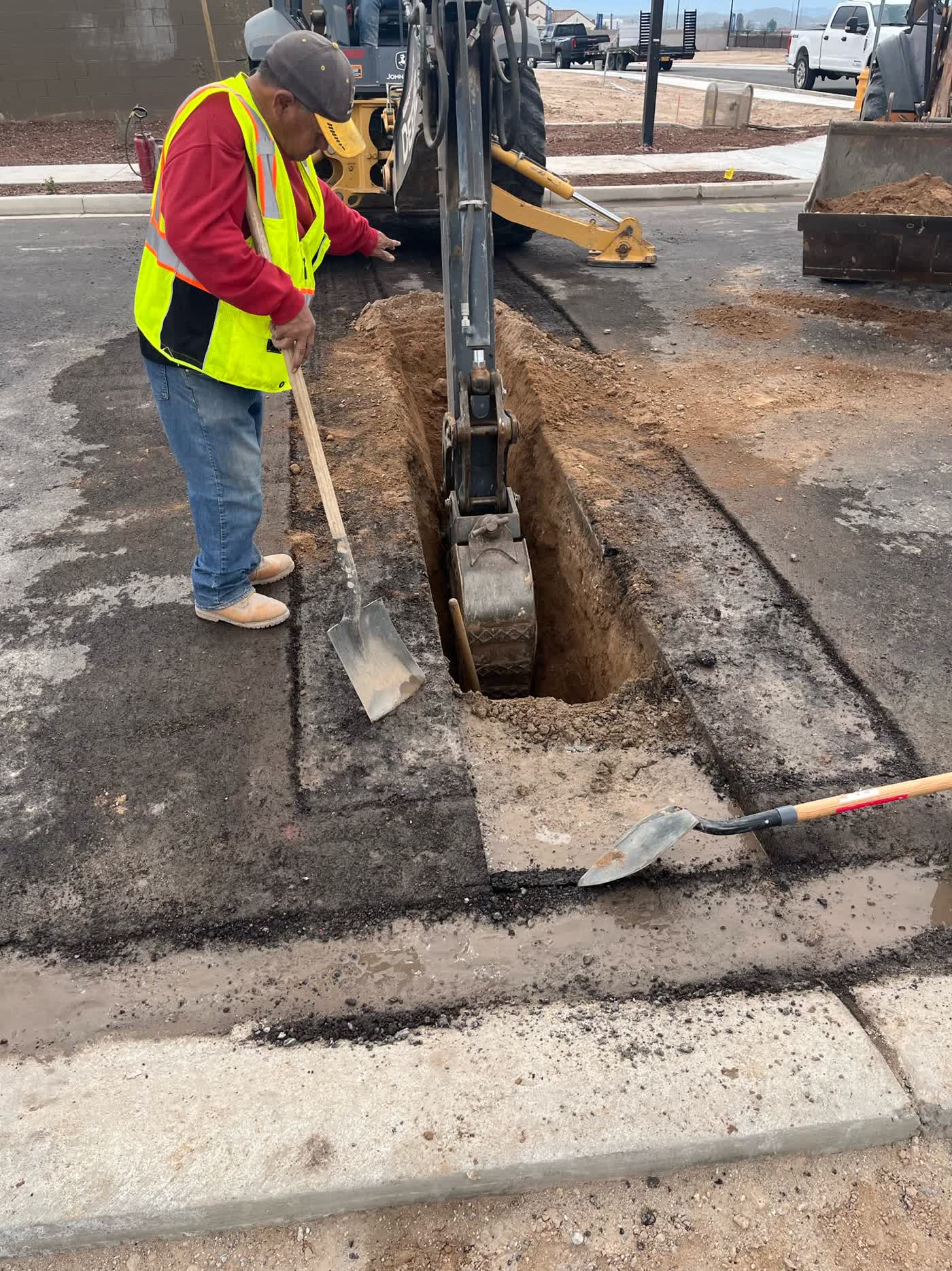 Backhoe and crew excavating an asphalt utility trench
