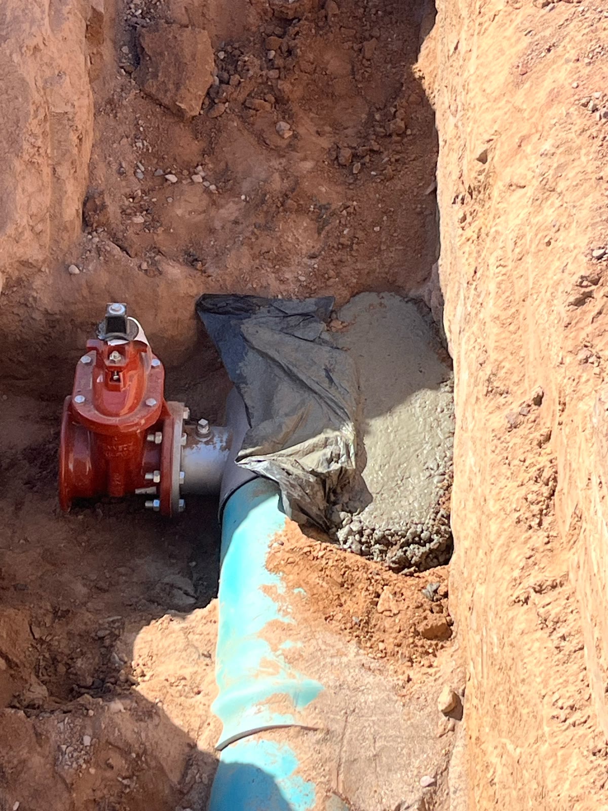 Red valve and concrete thrust block on blue water pipe in a trench